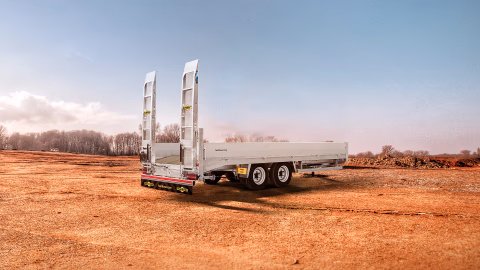Rimorchio Humbaur HBT a pianale ribassato con rampe alte, in cantiere per il trasporto di macchine operatrici.