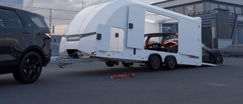 Rimorchio chiuso Brian James Race Sport con le porte laterali aperte e un’auto sportiva caricata, agganciato alla motrice.