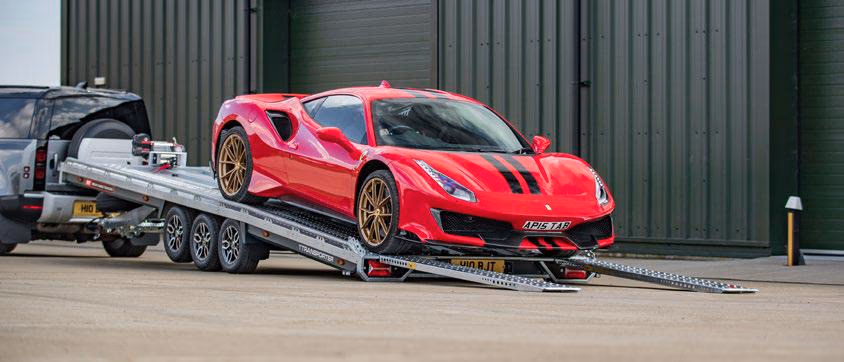 Ferrari rossa caricata su un rimorchio aperto Brian James T Transporter a tre assi con rampe posteriori abbassate.
